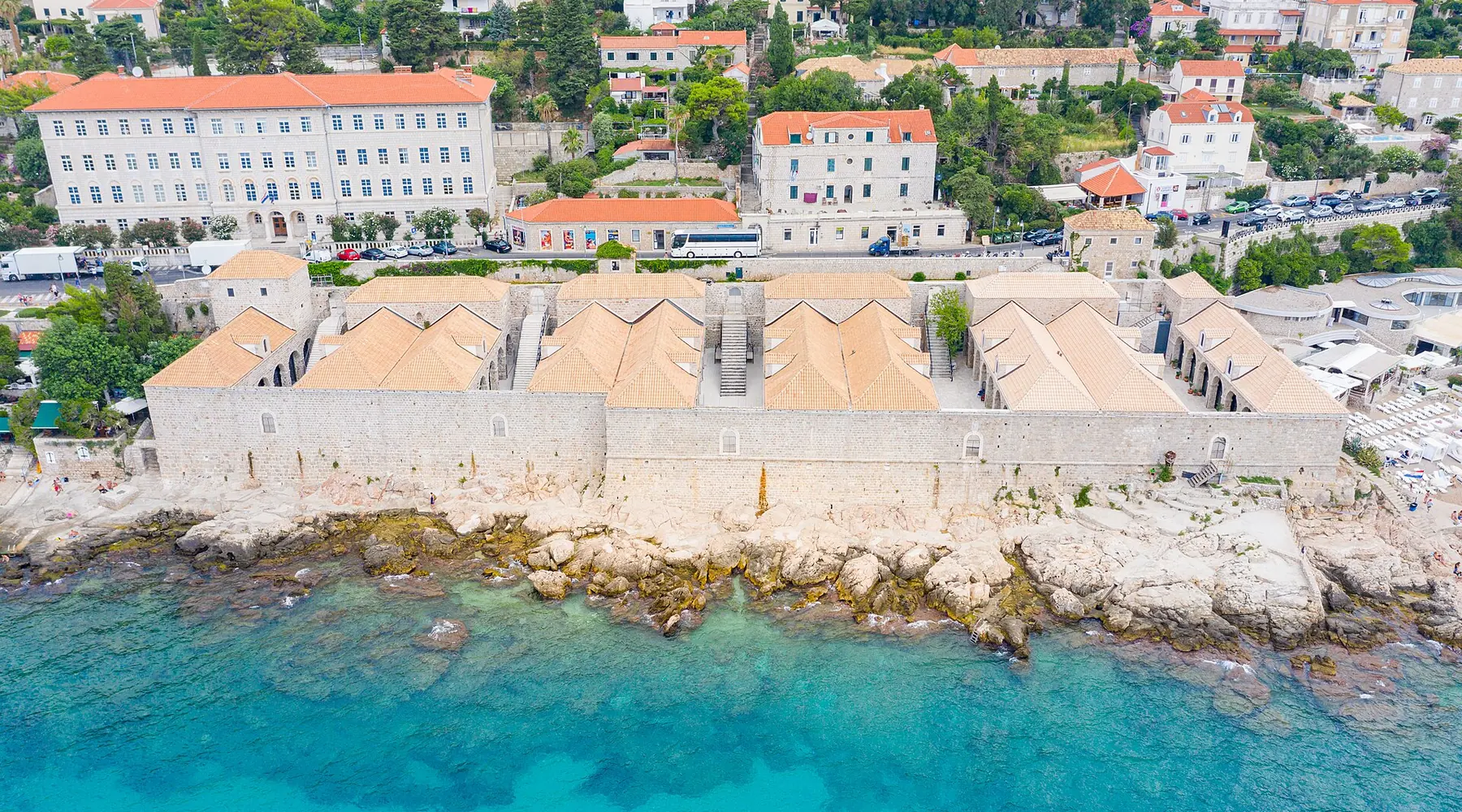 The Lazareti complex seen from above, a long stone range of terracotta roofs beside the turquoise Adriatic, with Dubrovnik's hillside behind.